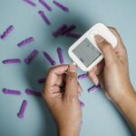 Top view of crop anonymous female diabetic measuring blood sugar with glucometer over scattered lancets