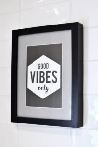Picture in wooden frame with Good Vibes Only inscription hanging on white tiled wall